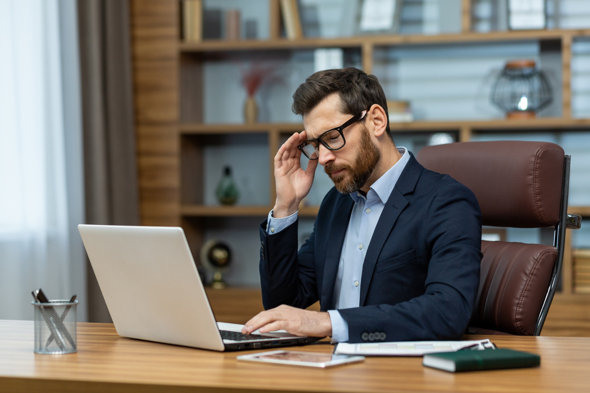 Frustrated administrator experiencing headache while sitting by desk with portable computer in